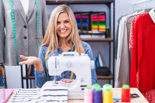 Blonde woman dressmaker designer using sew machine pointing aside with hands open palms showing copy space, presenting advertisement smiling excited happy