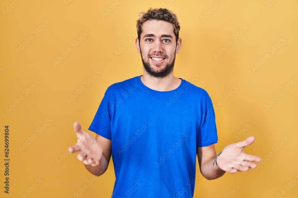 Hispanic man with beard standing over yellow background smiling cheerful offering hands giving assistance and acceptance. Hispanic man with beard standing over yellow background smiling cheerful offering hands giving assistance and acceptance.
