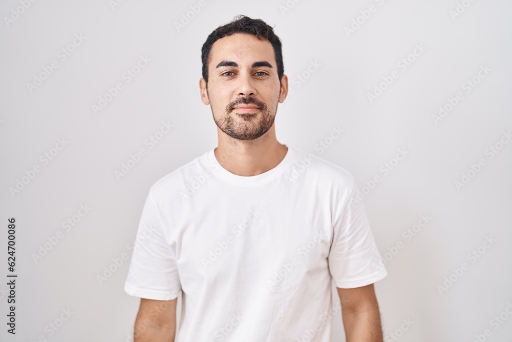 Handsome hispanic man standing over white background relaxed with serious expression on face. simple and natural looking at the camera. Handsome hispanic man standing over white background relaxed with serious expression on face. simple and natural looking at the camera.
