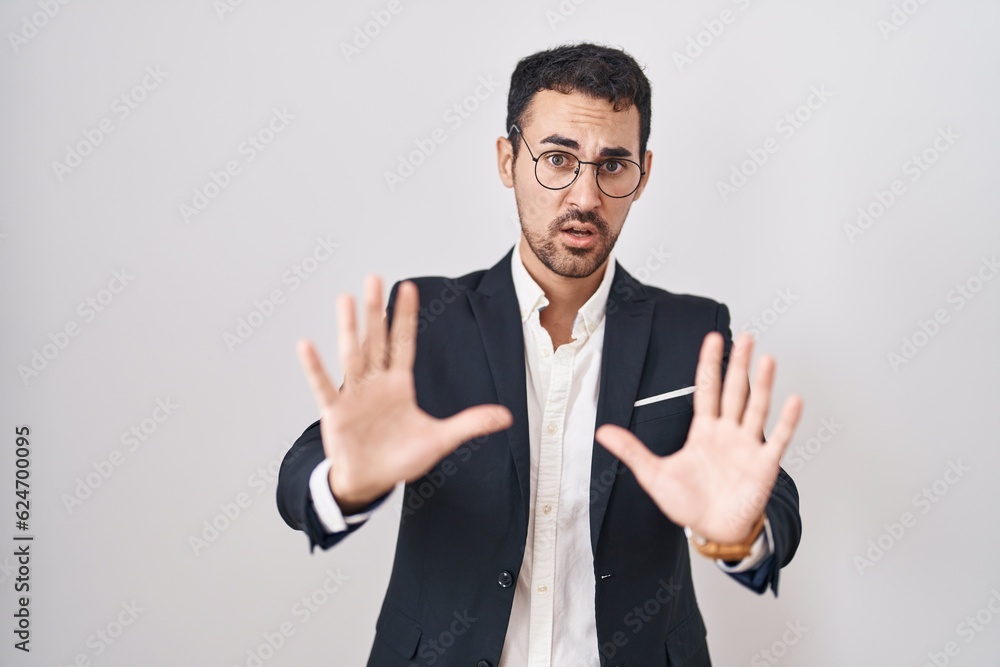 Handsome business hispanic man standing over white background afraid and terrified with fear expression stop gesture with hands, shouting in shock. panic concept.