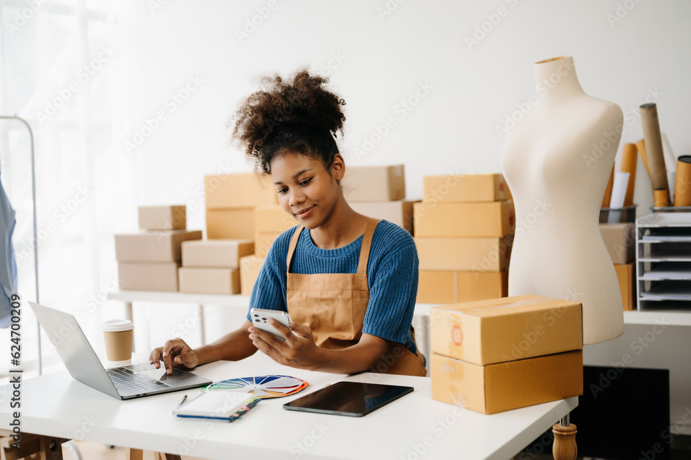 Startup small business SME, Entrepreneur owner African woman using smartphone or tablet taking receive and checking online purchase shopping order to preparing pack product box. in office. Startup small business SME, Entrepreneur owner African woman using smartphone or tablet taking receive and checking online purchase shopping order to preparing pack product box. in office.