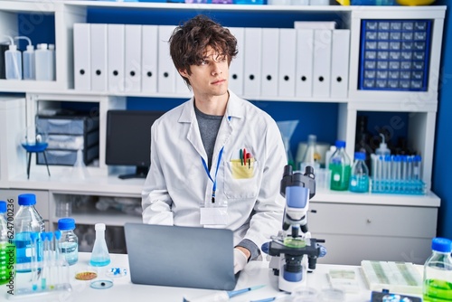 Young hispanic man scientist using laptop working at laboratory