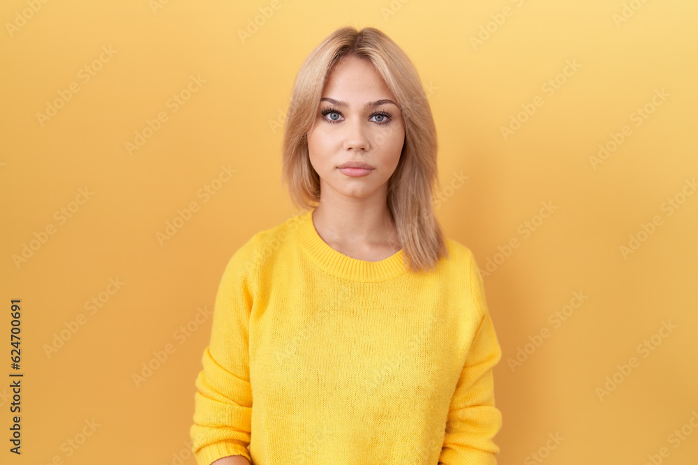 Young caucasian woman wearing yellow sweater relaxed with serious expression on face. simple and natural looking at the camera. Young caucasian woman wearing yellow sweater relaxed with serious expression on face. simple and natural looking at the camera.