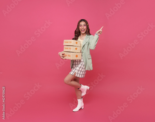 Happy Asian woman smiling holding package parcel box pointing finger isolated on pink copy space background.