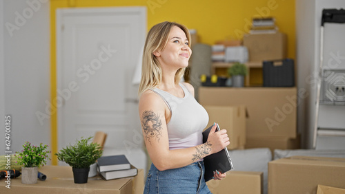 Young blonde woman holding laptop smiling at new home