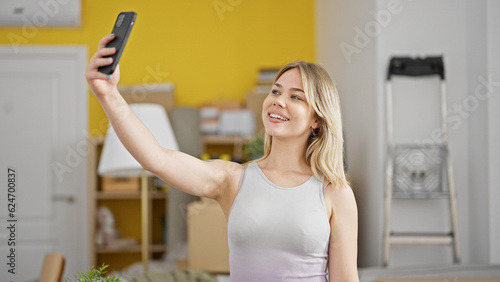 Young blonde woman make selfie by smartphone standing at new home