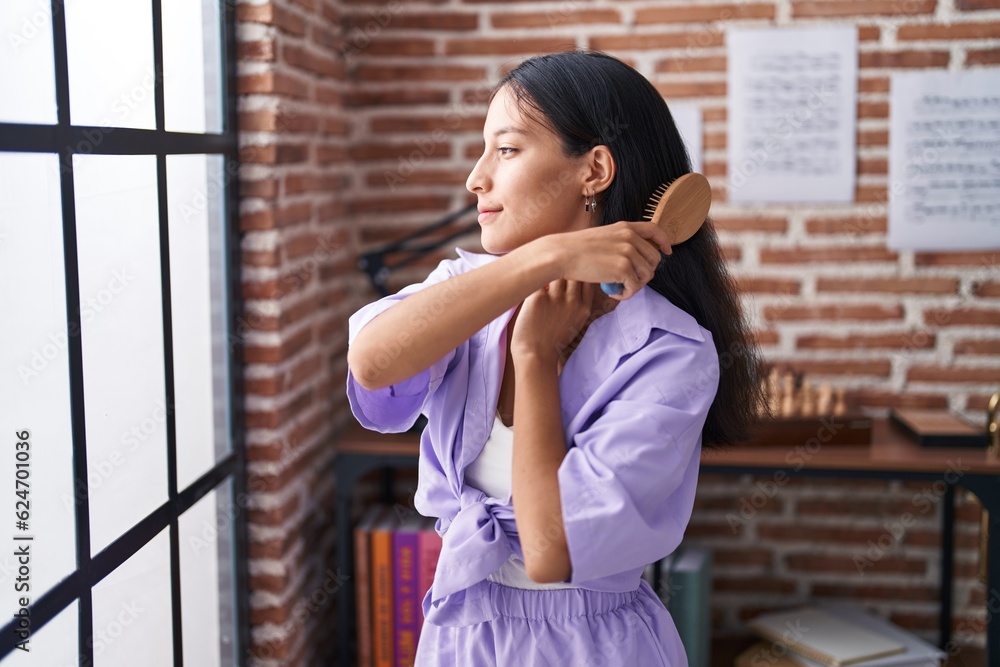 Young beautiful hispanic woman combing hair standing at home