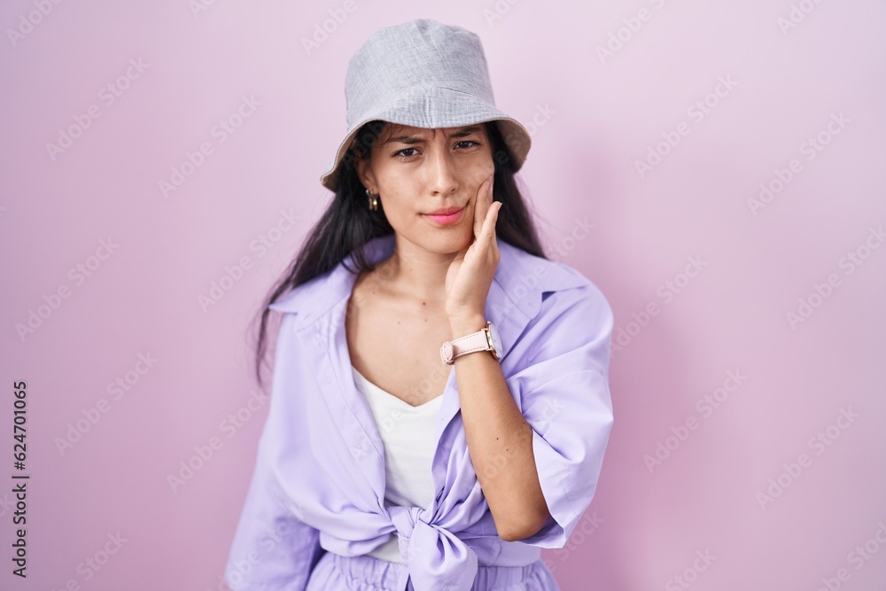 Young hispanic woman standing over pink background wearing hat touching mouth with hand with painful expression because of toothache or dental illness on teeth. dentist Young hispanic woman standing over pink background wearing hat touching mouth with hand with painful expression because of toothache or dental illness on teeth. dentist
