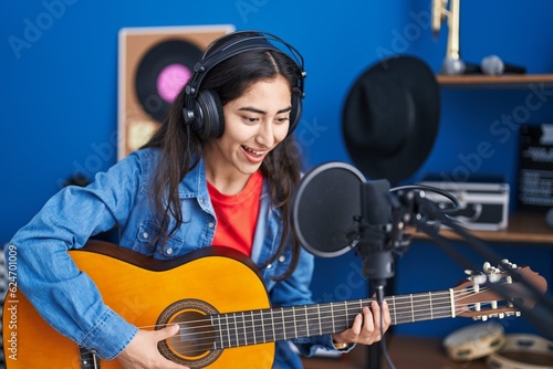Young hispanic girl musician singing song playing classical guitar at music studio
