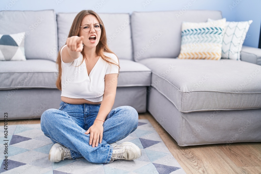 Young caucasian woman sitting on the floor at the living room pointing displeased and frustrated to the camera, angry and furious with you Young caucasian woman sitting on the floor at the living room pointing displeased and frustrated to the camera, angry and furious with you