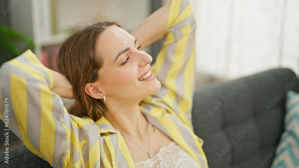 Young blonde woman relaxed with hands on head sitting on sofa smiling at home Young blonde woman relaxed with hands on head sitting on sofa smiling at home