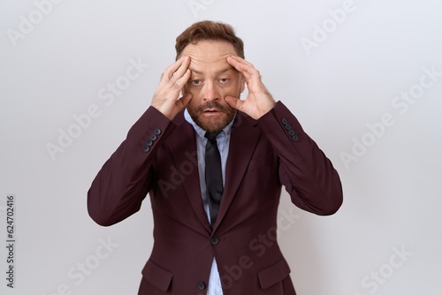 Middle age business man with beard wearing suit and tie trying to open eyes with fingers, sleepy and tired for morning fatigue