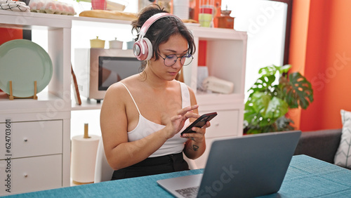 Young beautiful hispanic woman listening to music sitting on table at dinning room