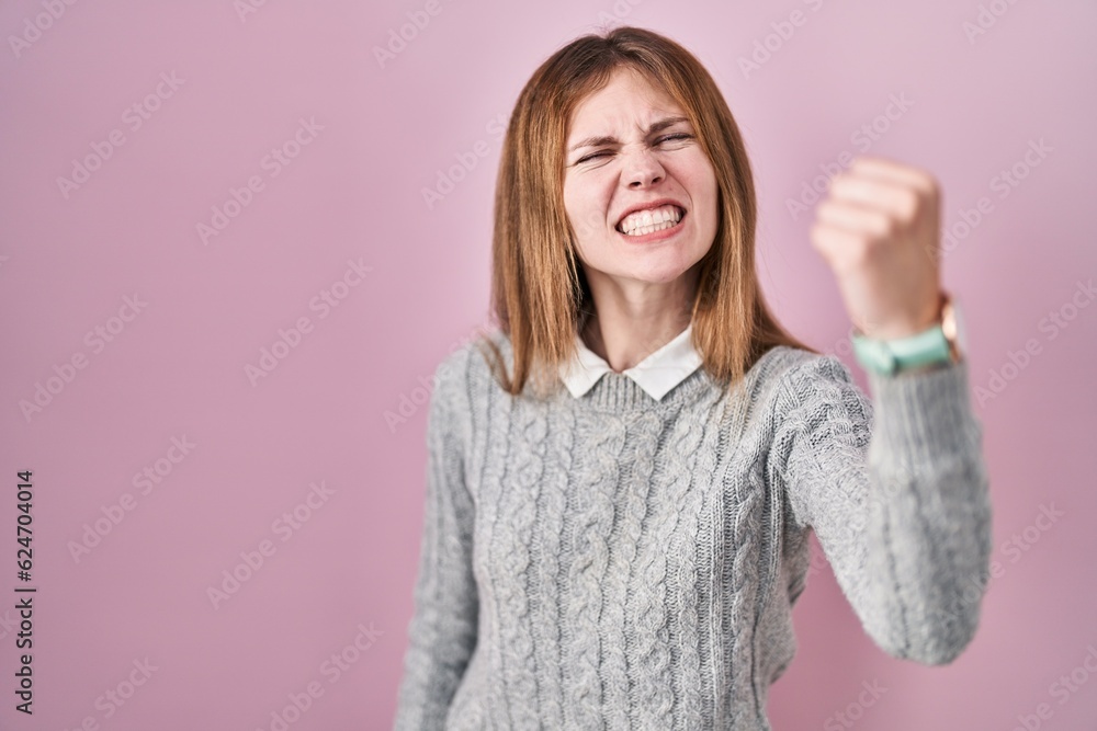 Beautiful woman standing over pink background angry and mad raising fist frustrated and furious while shouting with anger. rage and aggressive concept. Beautiful woman standing over pink background angry and mad raising fist frustrated and furious while shouting with anger. rage and aggressive concept.