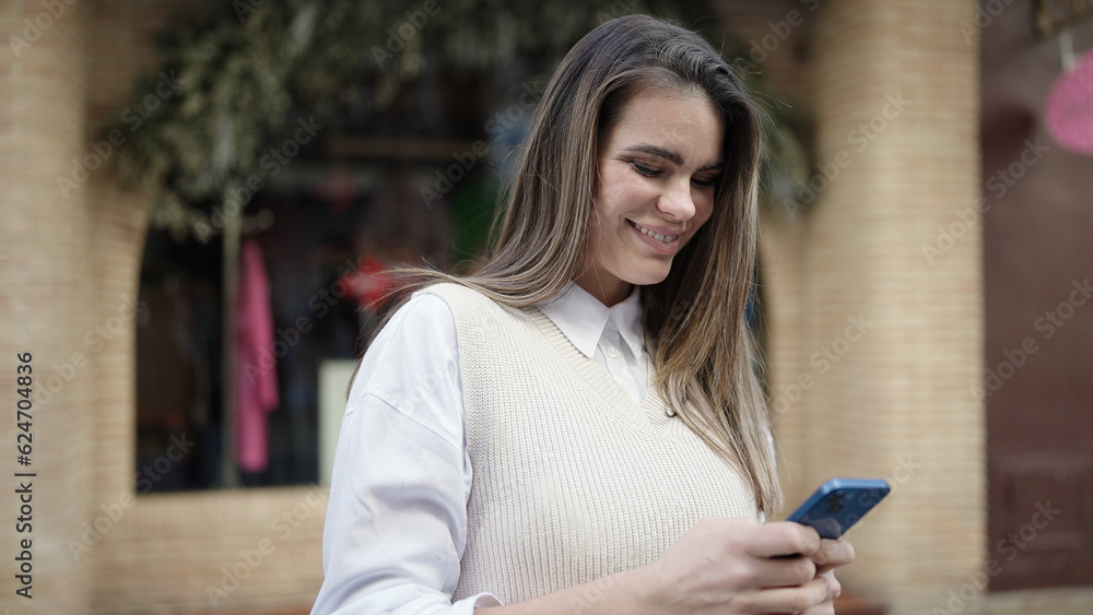 Young beautiful hispanic woman using smartphone smiling at street