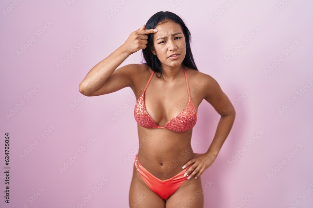 Hispanic woman wearing bikini pointing unhappy to pimple on forehead, ugly infection of blackhead. acne and skin problem Hispanic woman wearing bikini pointing unhappy to pimple on forehead, ugly infection of blackhead. acne and skin problem