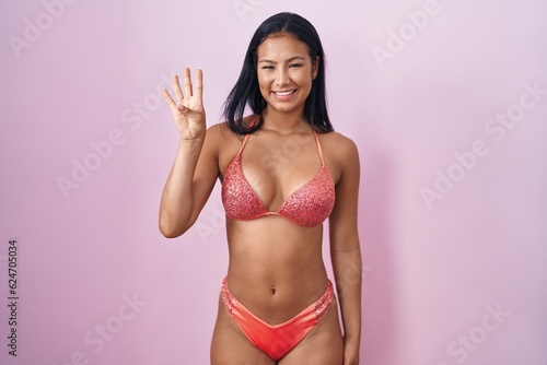 Hispanic woman wearing bikini showing and pointing up with fingers number four while smiling confident and happy.