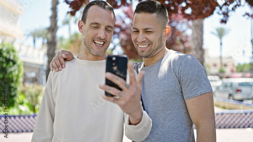 Two men couple smiling confident using smartphone at park