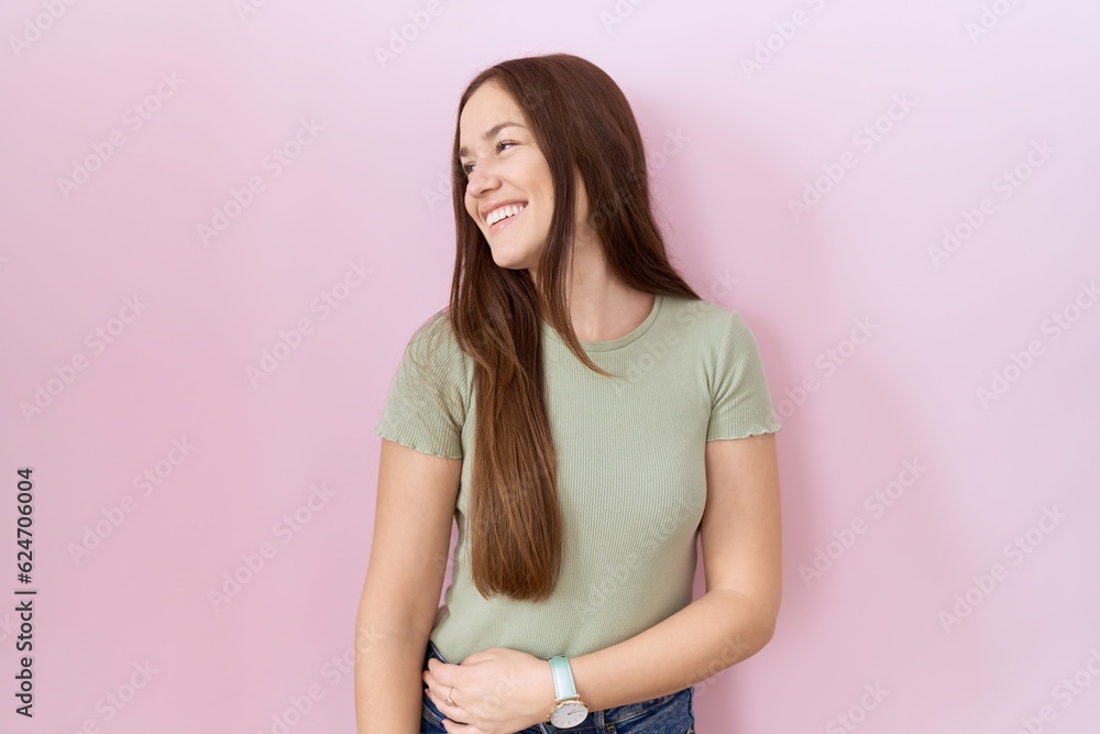 Beautiful brunette woman standing over pink background looking away to side with smile on face, natural expression. laughing confident. Beautiful brunette woman standing over pink background looking away to side with smile on face, natural expression. laughing confident.