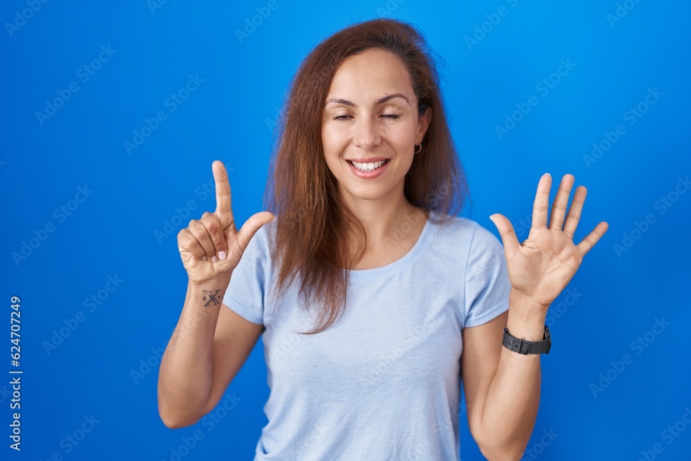 Brunette woman standing over blue background showing and pointing up with fingers number seven while smiling confident and happy. Brunette woman standing over blue background showing and pointing up with fingers number seven while smiling confident and happy.
