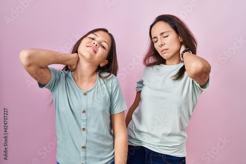 Young mother and daughter standing over pink background suffering of neck ache injury, touching neck with hand, muscular pain