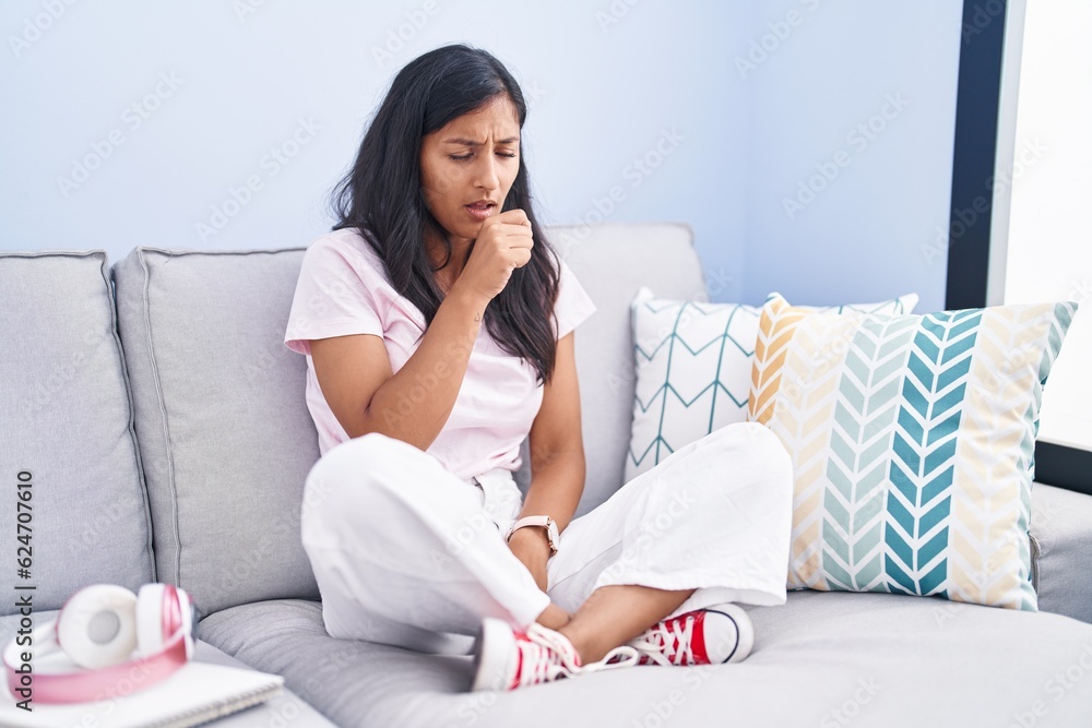 Young hispanic woman sitting on the sofa at home feeling unwell and coughing as symptom for cold or bronchitis. health care concept. Young hispanic woman sitting on the sofa at home feeling unwell and coughing as symptom for cold or bronchitis. health care concept.