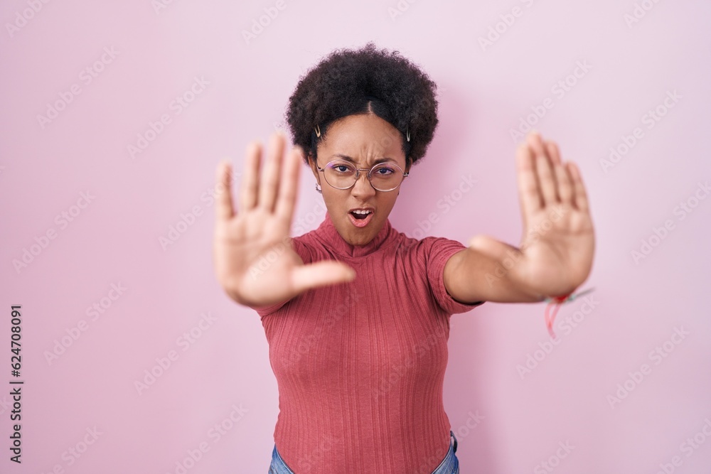Beautiful african woman with curly hair standing over pink background doing stop gesture with hands palms, angry and frustration expression Beautiful african woman with curly hair standing over pink background doing stop gesture with hands palms, angry and frustration expression