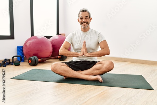 Middle age grey-haired man smiling confident training yoga at sport center