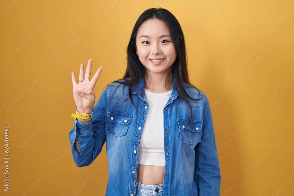 Young asian woman standing over yellow background showing and pointing up with fingers number four while smiling confident and happy. Young asian woman standing over yellow background showing and pointing up with fingers number four while smiling confident and happy.