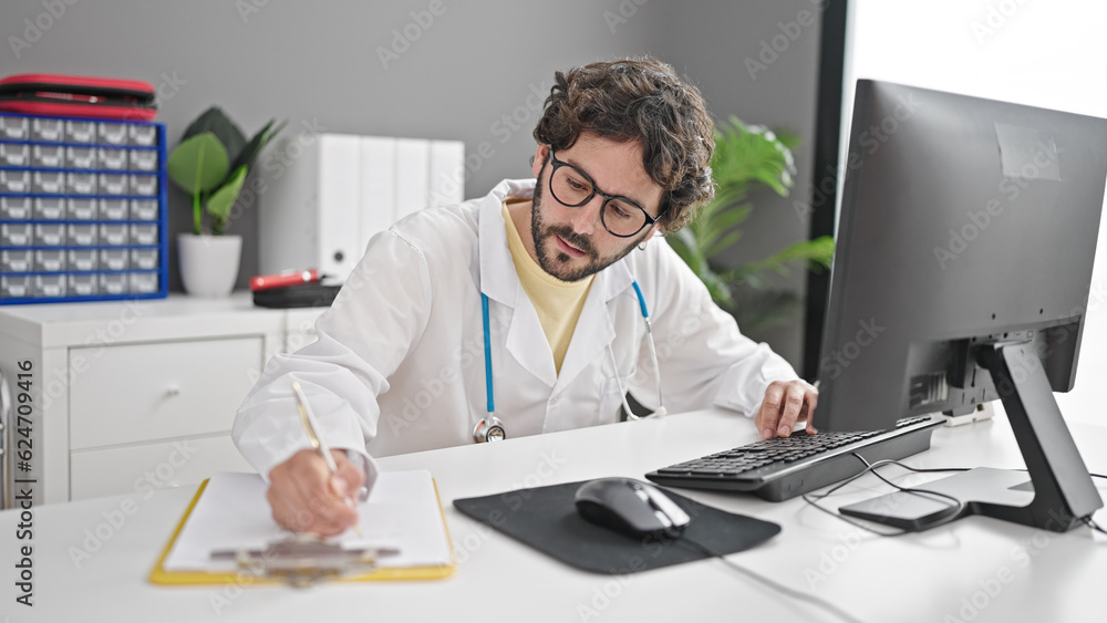 Young hispanic man doctor using computer writing medical report at clinic