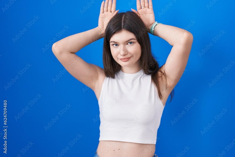Young caucasian woman standing over blue background doing bunny ears gesture with hands palms looking cynical and skeptical. easter rabbit concept.
