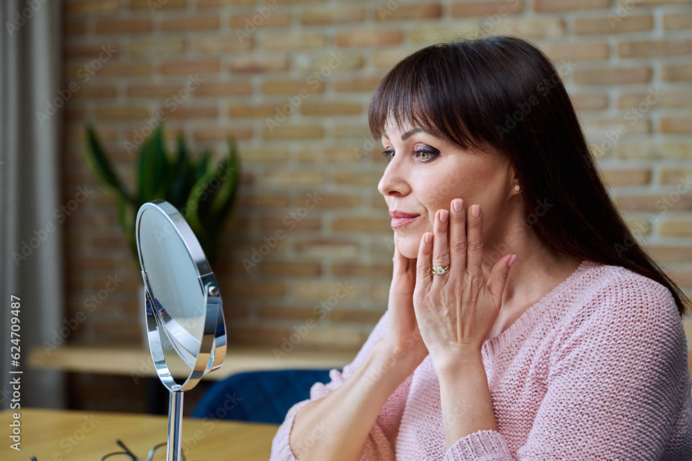 Middle aged beautiful woman looking at her face in mirror Middle aged beautiful woman looking at her face in mirror
