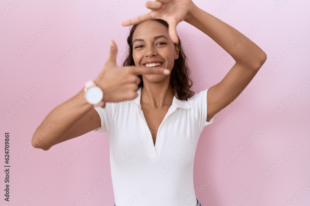 Fototapeta premium Young hispanic woman wearing casual white t shirt smiling making frame with hands and fingers with happy face. creativity and photography concept.