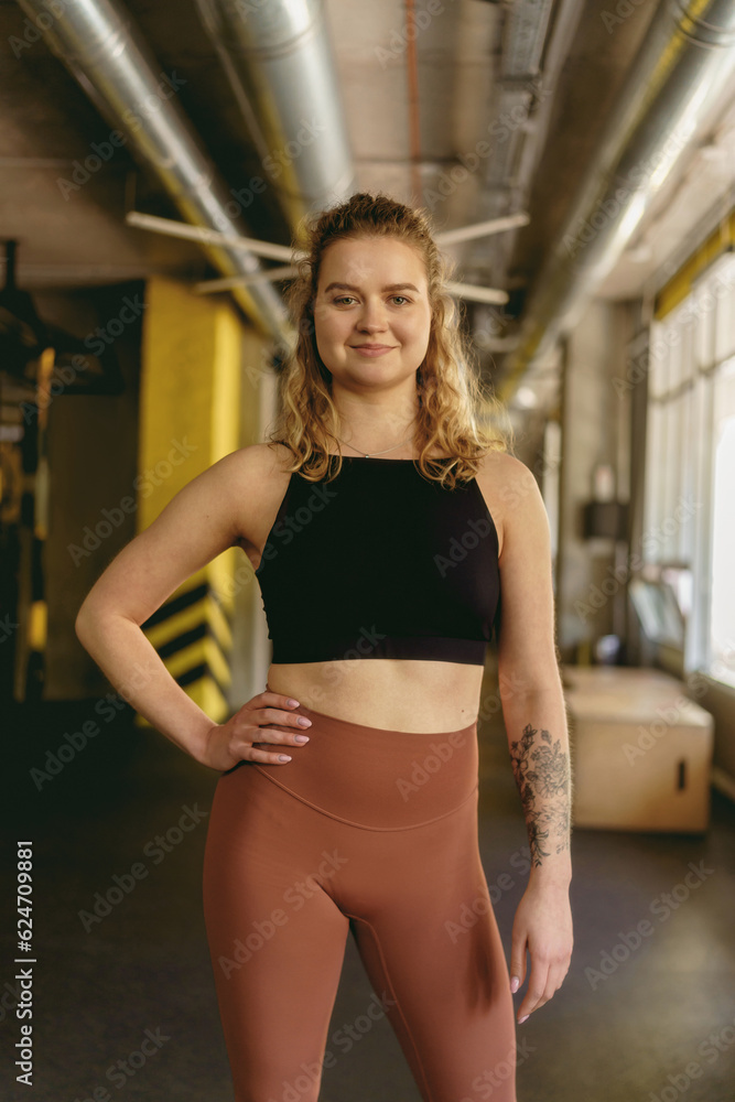 Portrait of fit athletic woman fitness trainer or coach smiling at the camera while standing in gym