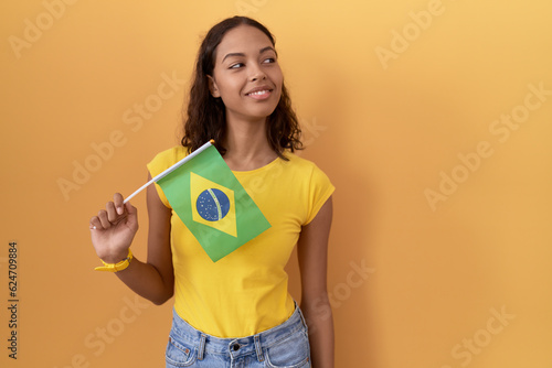 Young hispanic woman holding brazil flag looking away to side with smile on face, natural expression. laughing confident.