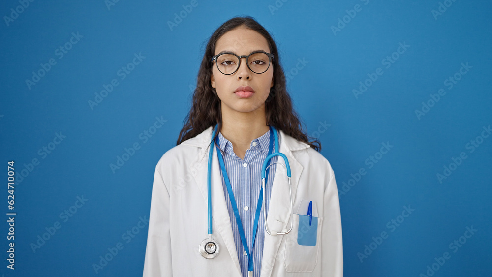 Young beautiful hispanic woman doctor standing with serious expression over isolated blue background Young beautiful hispanic woman doctor standing with serious expression over isolated blue background