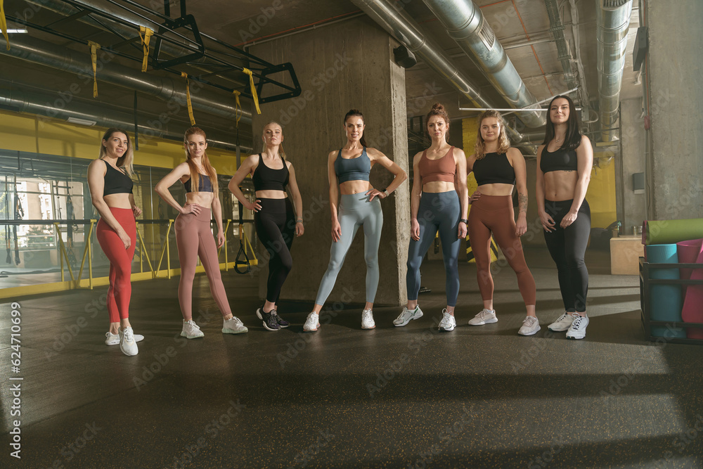 Group of athletic female fitness instructors standing in Gym and looking at camera with smile 