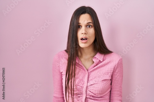 Young hispanic woman standing over pink background afraid and shocked with surprise and amazed expression, fear and excited face. © Krakenimages.com