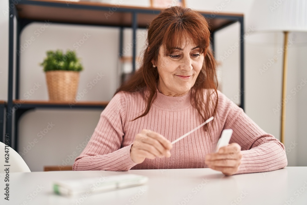 Middle age woman holding antigen covid-19 test sitting on table at home Middle age woman holding antigen covid-19 test sitting on table at home