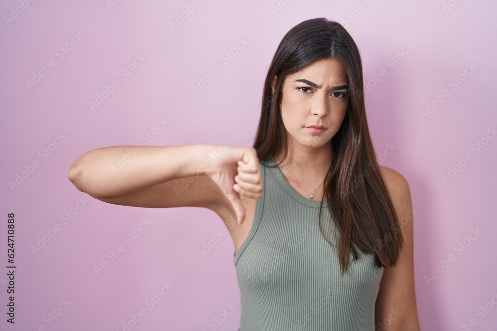 Hispanic woman standing over pink background looking unhappy and angry showing rejection and negative with thumbs down gesture. bad expression. Hispanic woman standing over pink background looking unhappy and angry showing rejection and negative with thumbs down gesture. bad expression.