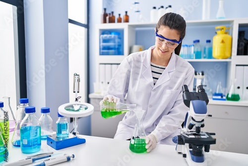 Young beautiful hispanic woman scientist pouring liquid on test tube at laboratory