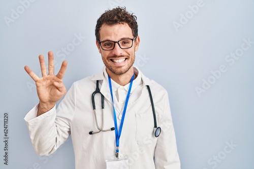 Young hispanic man wearing doctor uniform and stethoscope showing and pointing up with fingers number four while smiling confident and happy.