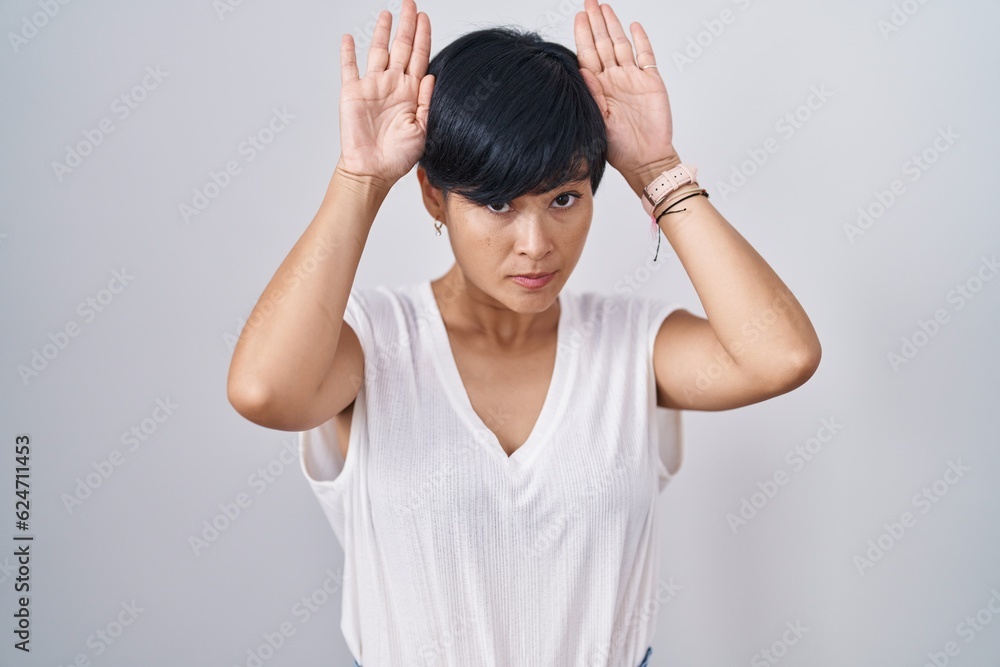Young asian woman with short hair standing over isolated background doing bunny ears gesture with hands palms looking cynical and skeptical. easter rabbit concept. Young asian woman with short hair standing over isolated background doing bunny ears gesture with hands palms looking cynical and skeptical. easter rabbit concept.