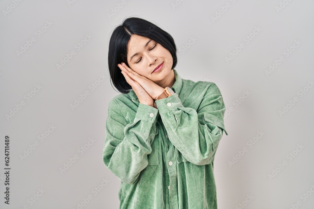 Young asian woman standing over white background sleeping tired dreaming and posing with hands together while smiling with closed eyes. Young asian woman standing over white background sleeping tired dreaming and posing with hands together while smiling with closed eyes.