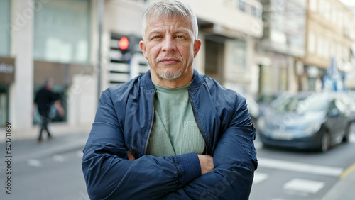 Middle age grey-haired man standing with serious expression and arms crossed gesture at street