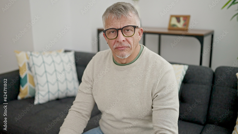 Middle age grey-haired man sitting on sofa with relaxed expression at home Middle age grey-haired man sitting on sofa with relaxed expression at home