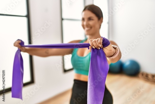 Young beautiful hispanic woman smiling confident using elastic band training at sport center