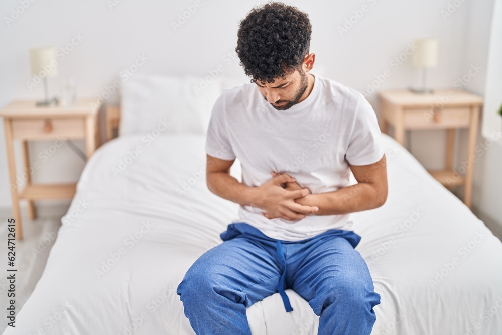 Young arab man suffering for stomachache sitting on bed at bedroom Young arab man suffering for stomachache sitting on bed at bedroom