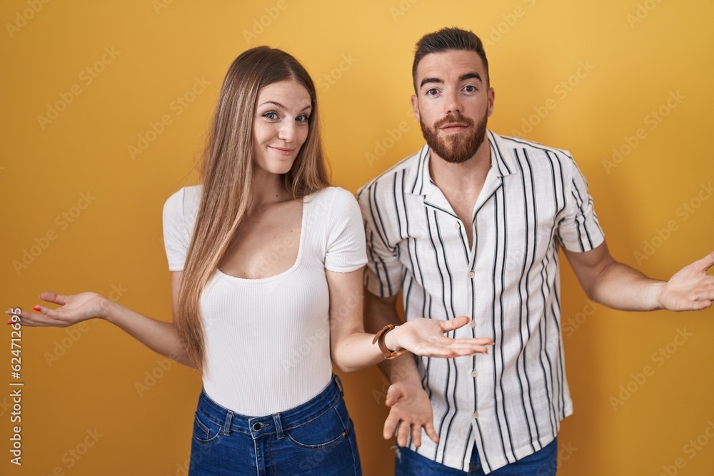Young couple standing over yellow background clueless and confused with open arms, no idea concept. Young couple standing over yellow background clueless and confused with open arms, no idea concept.