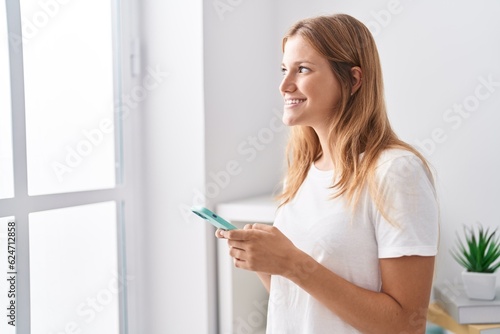 Young blonde girl smiling confident using smartphone at home